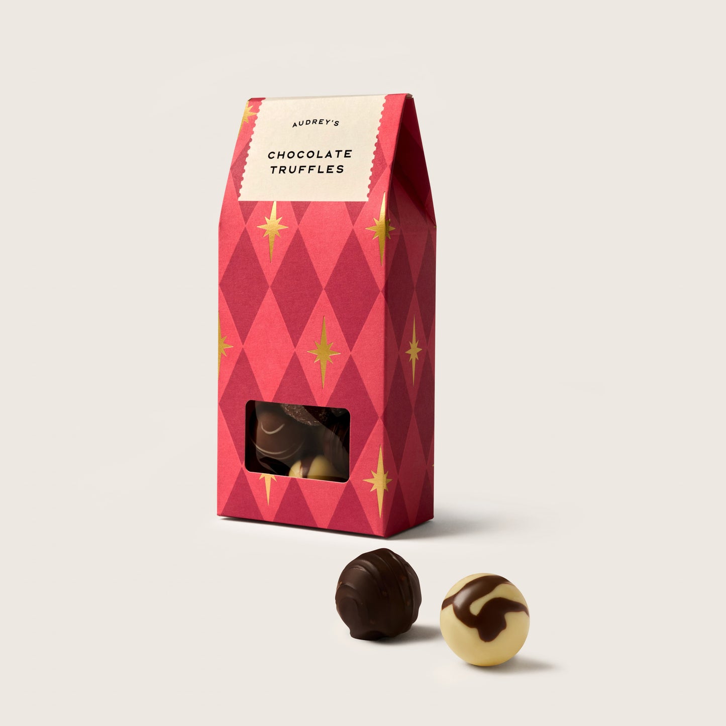 Red patterned box of chocolate truffles with two truffles on a light background
