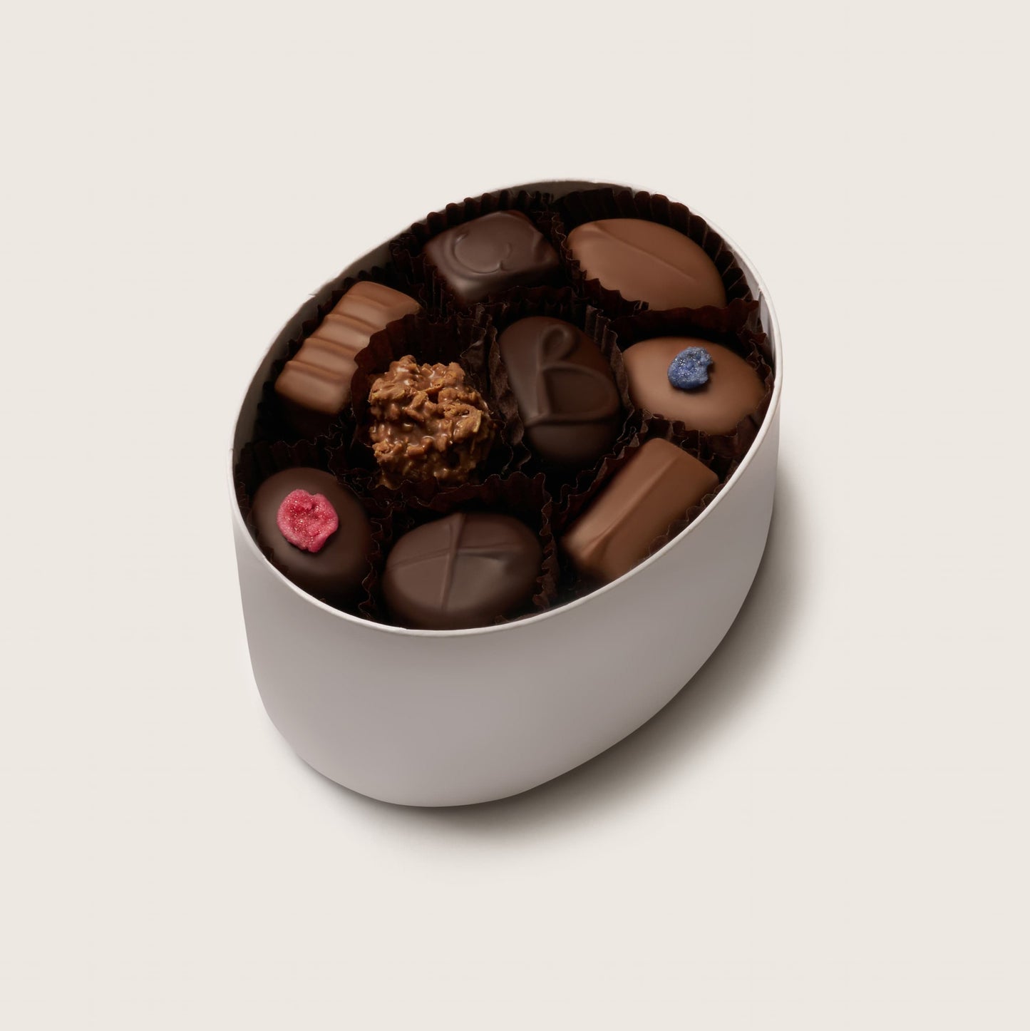 Assorted chocolates in a white container on a light beige background