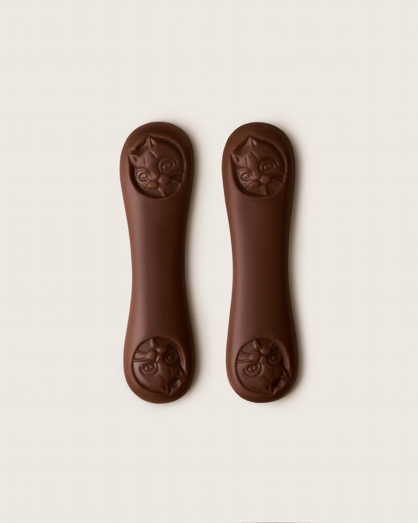 Two brown dog chew toys with cat face designs on a white background