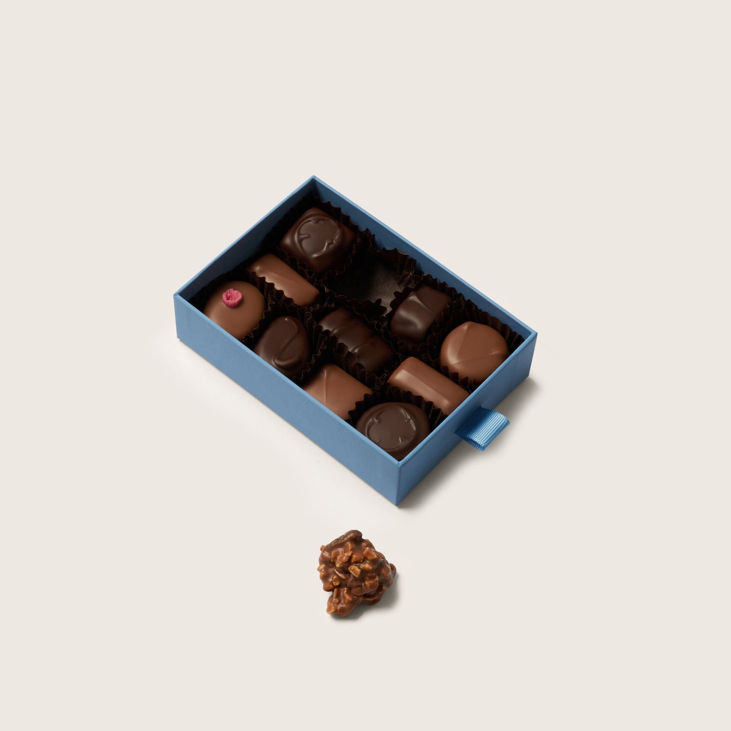 Box of chocolates with a single chocolate on a light beige background