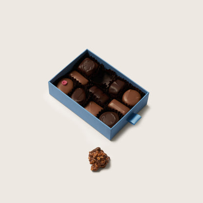 Box of chocolates with a single chocolate on a light beige background