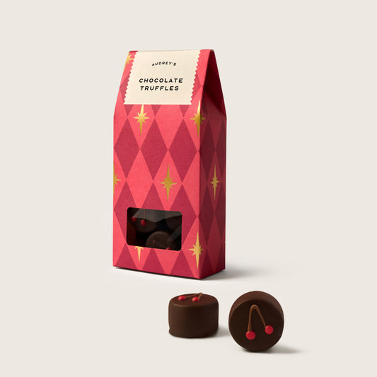 Red patterned box of chocolate truffles with two truffles on a white background