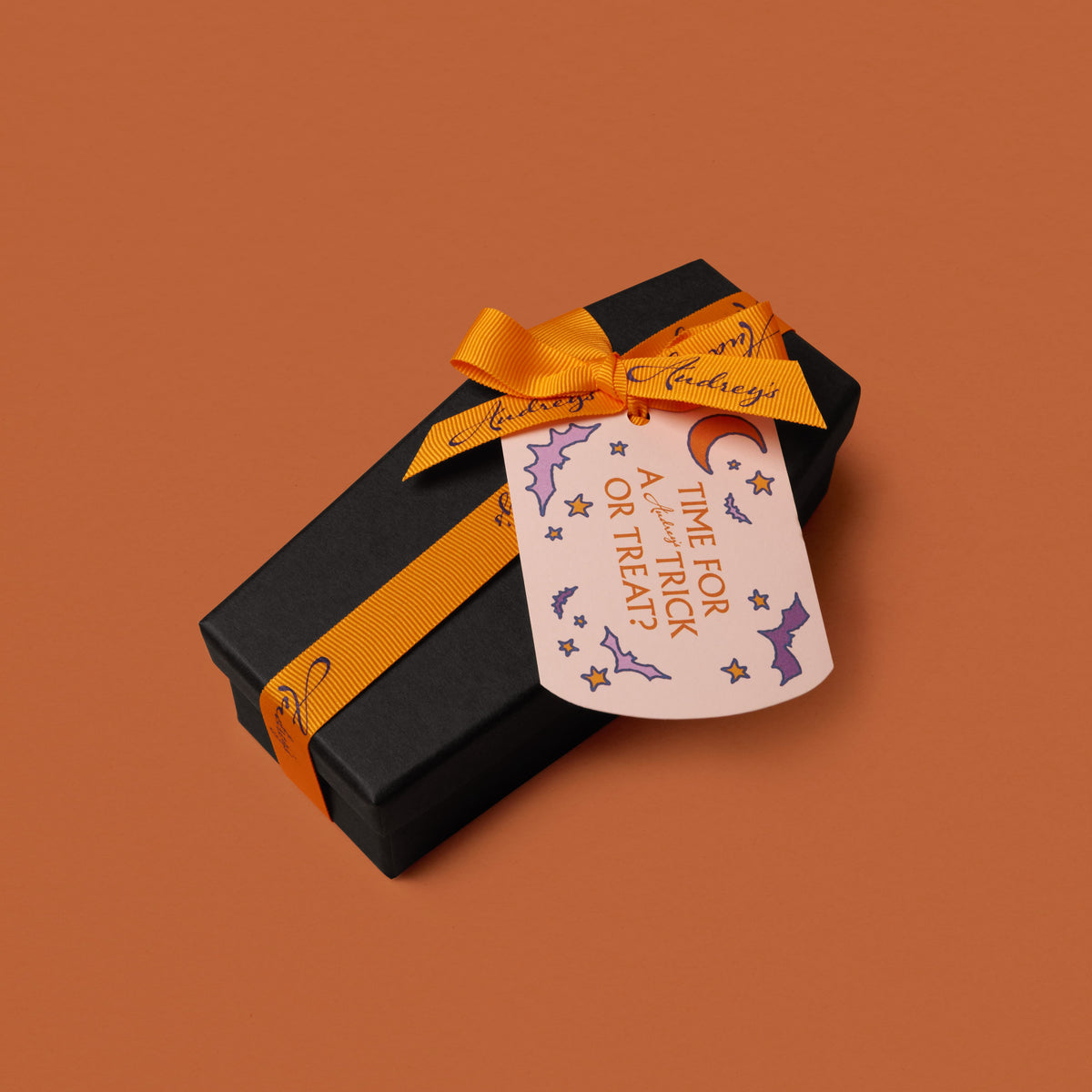 Black gift box with orange ribbon and Halloween-themed card on a brown background