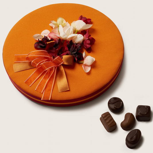 Decorative round orange plate with floral arrangement and chocolate candies on a light background