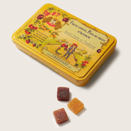 Yellow tin box with decorative design and candied fruits on a light beige background