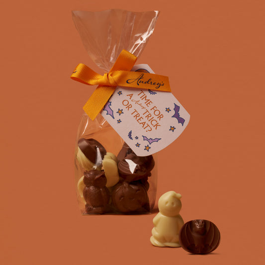 Halloween-themed chocolate treats in a clear bag with an orange ribbon on an orange background.