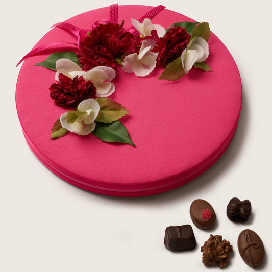 Pink gift box with floral decorations and chocolates on a white background