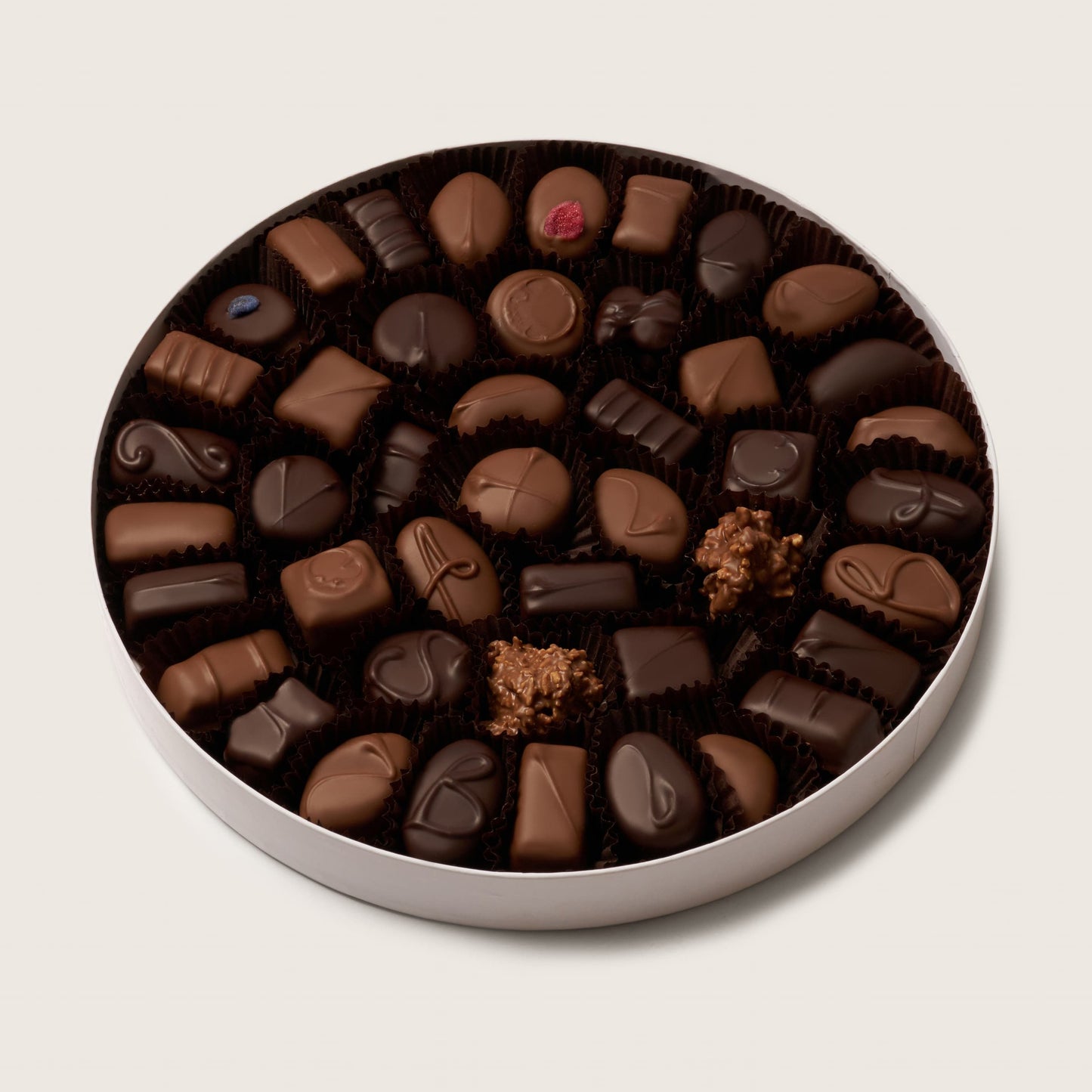 Assorted chocolate truffles in a round tin on a light beige background