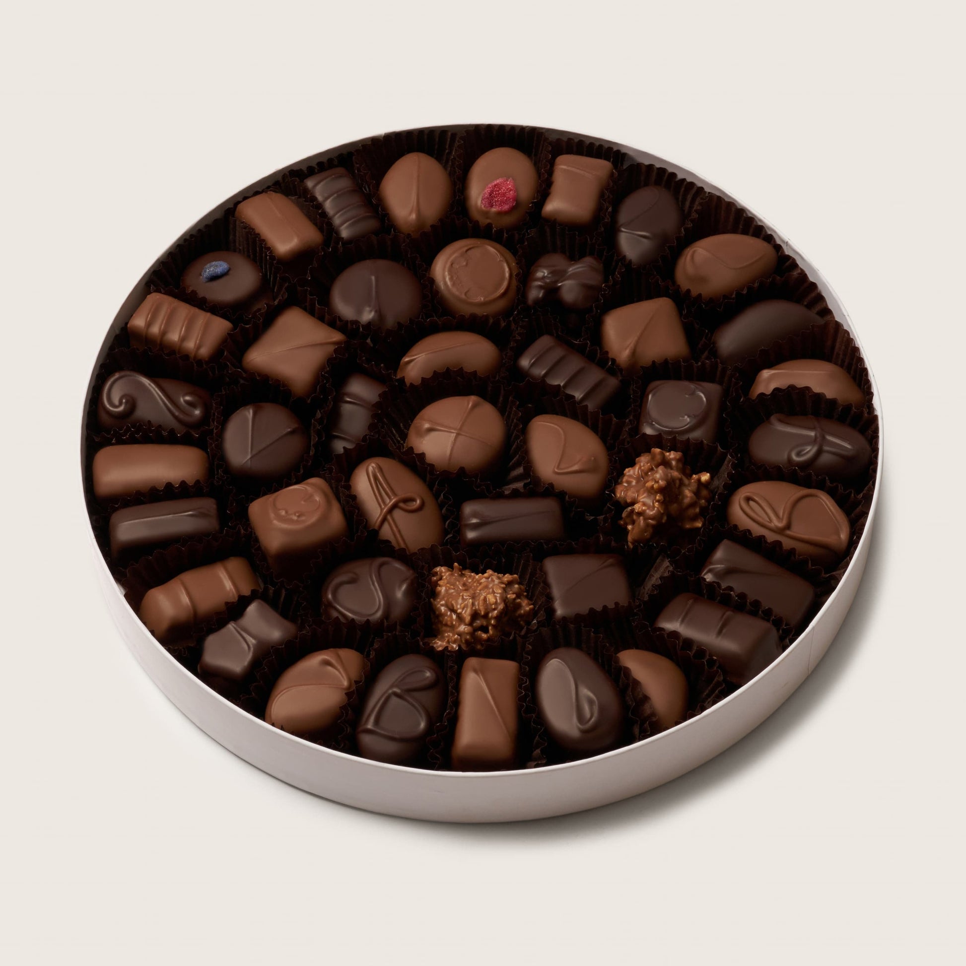 Assorted chocolate truffles in a round tin on a light beige background