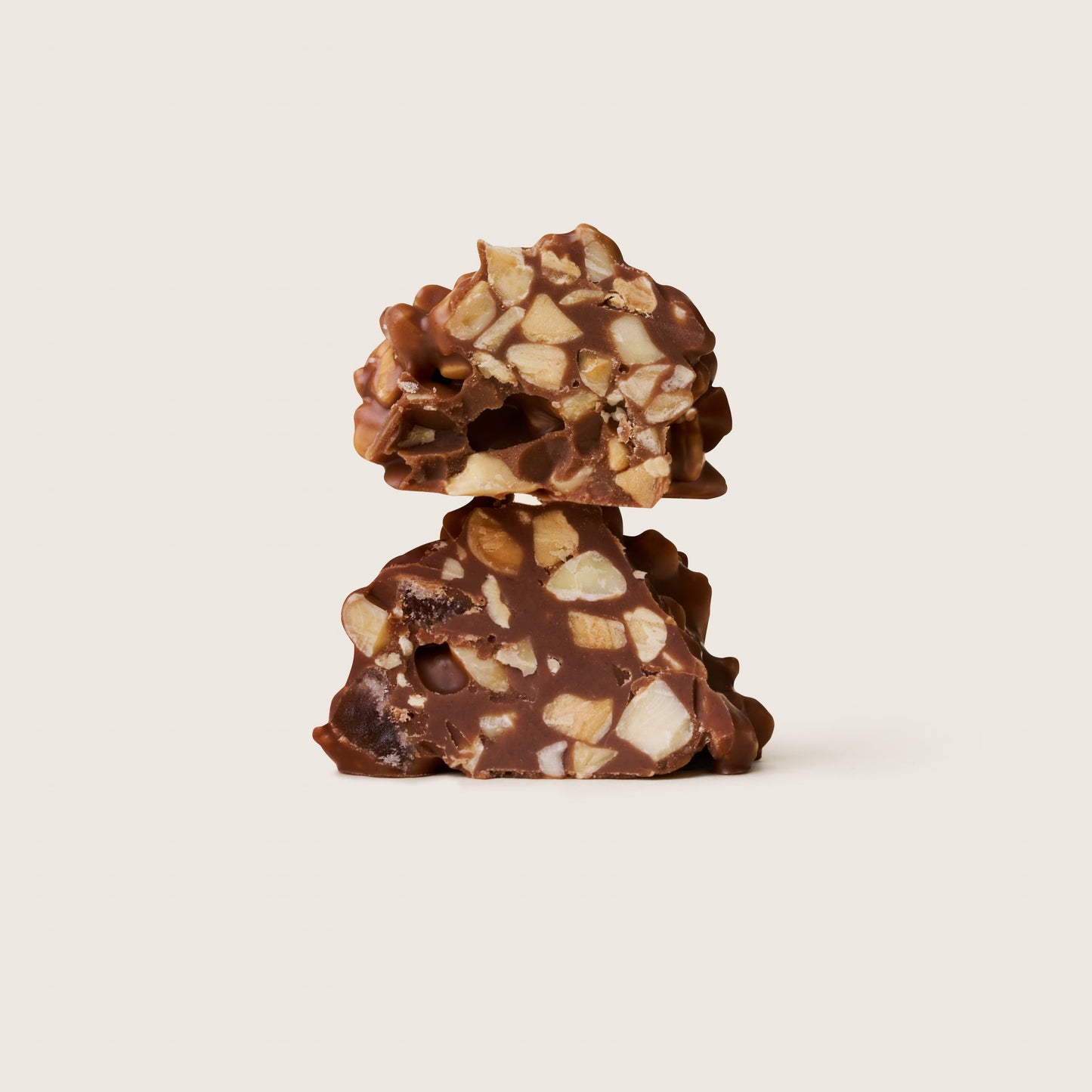 Two pieces of chocolate candy with nuts on a beige background