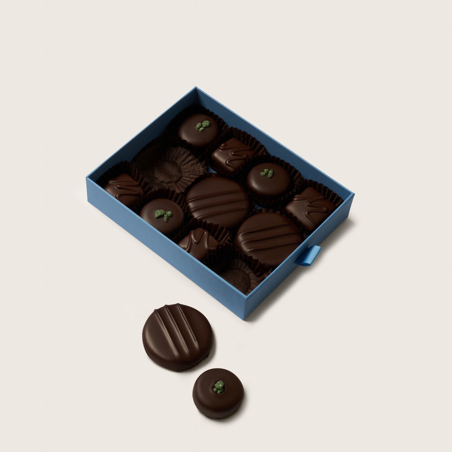 Box of dark chocolates with a few outside on a light beige background