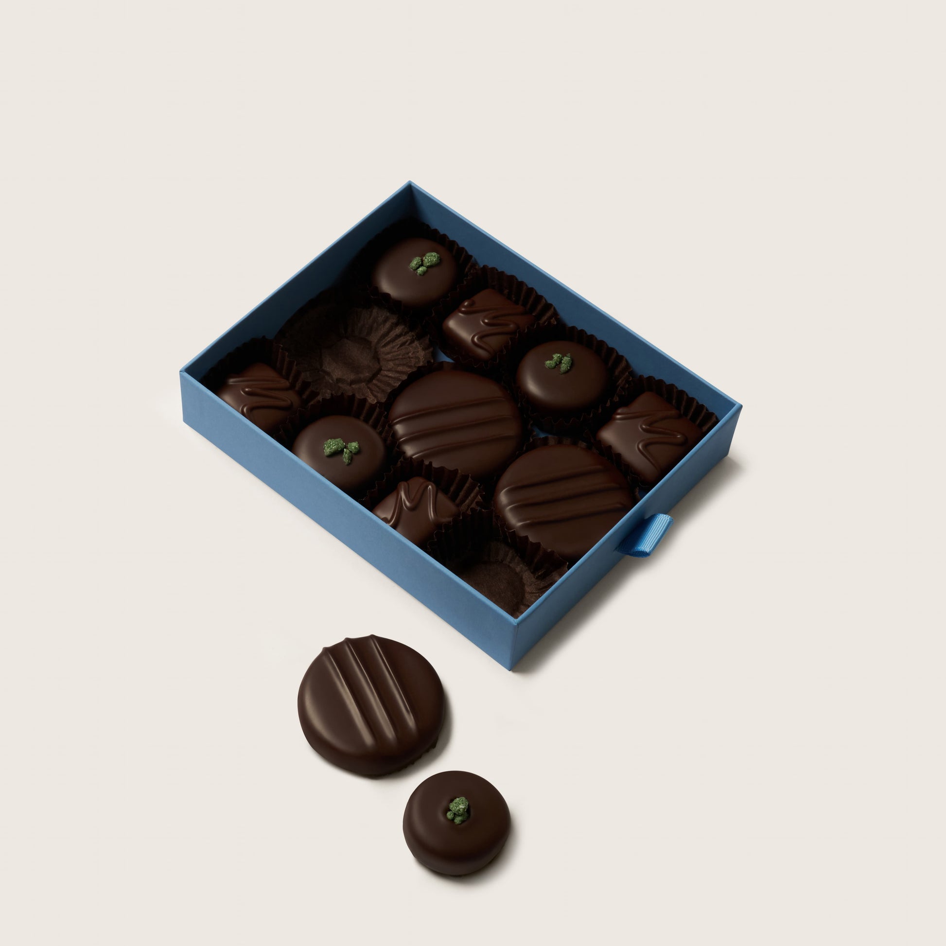 Box of dark chocolates with a few outside on a light beige background