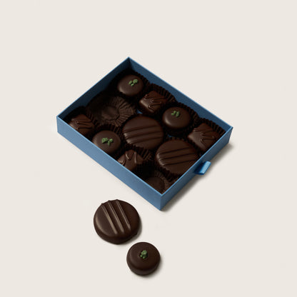 Box of dark chocolates with a few outside on a light beige background