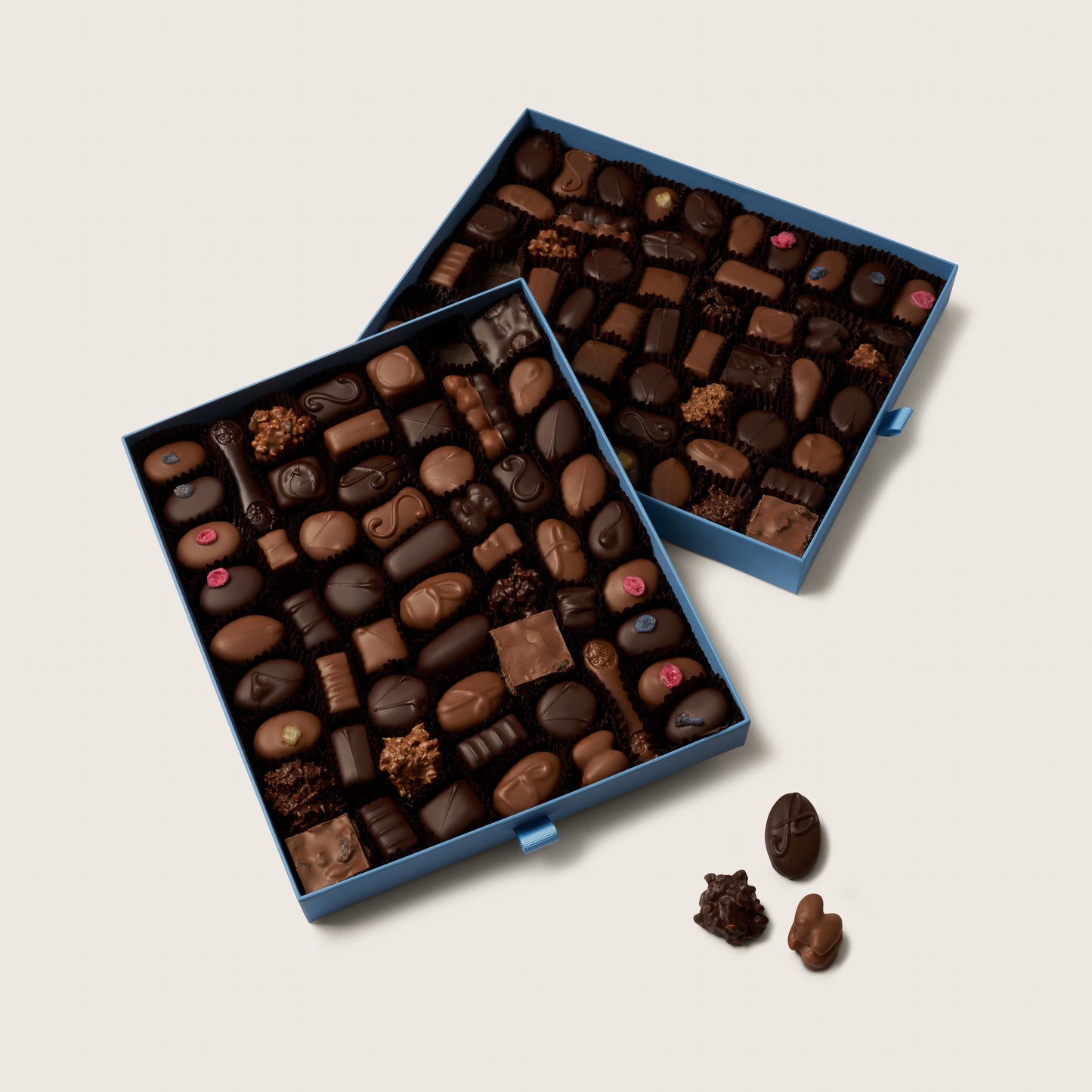 Two blue boxes filled with assorted chocolates on a light gray background
