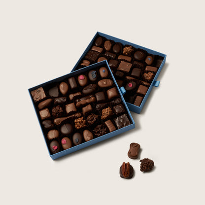 Two blue boxes filled with assorted chocolates on a light beige background