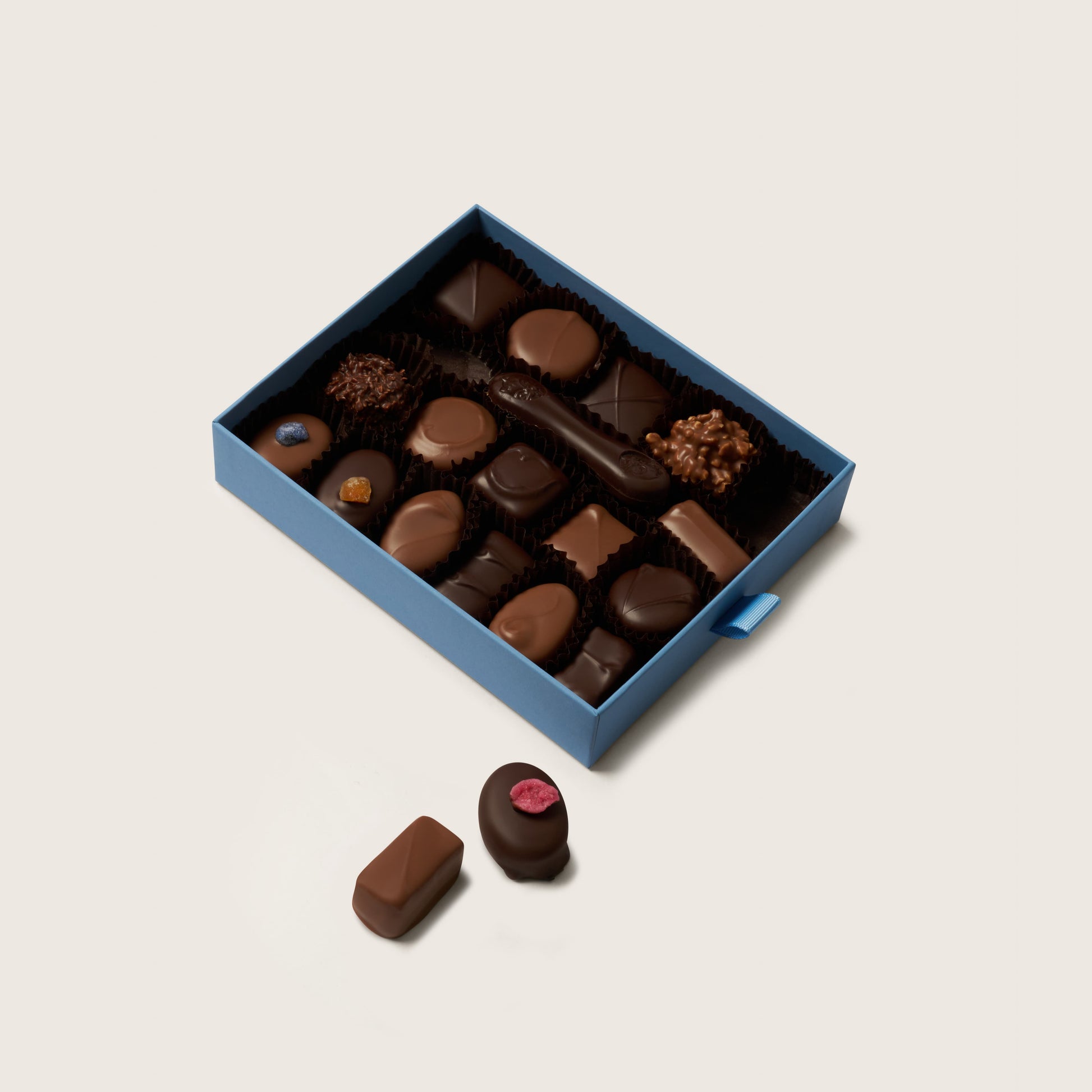 Open box of assorted chocolates on a light beige background