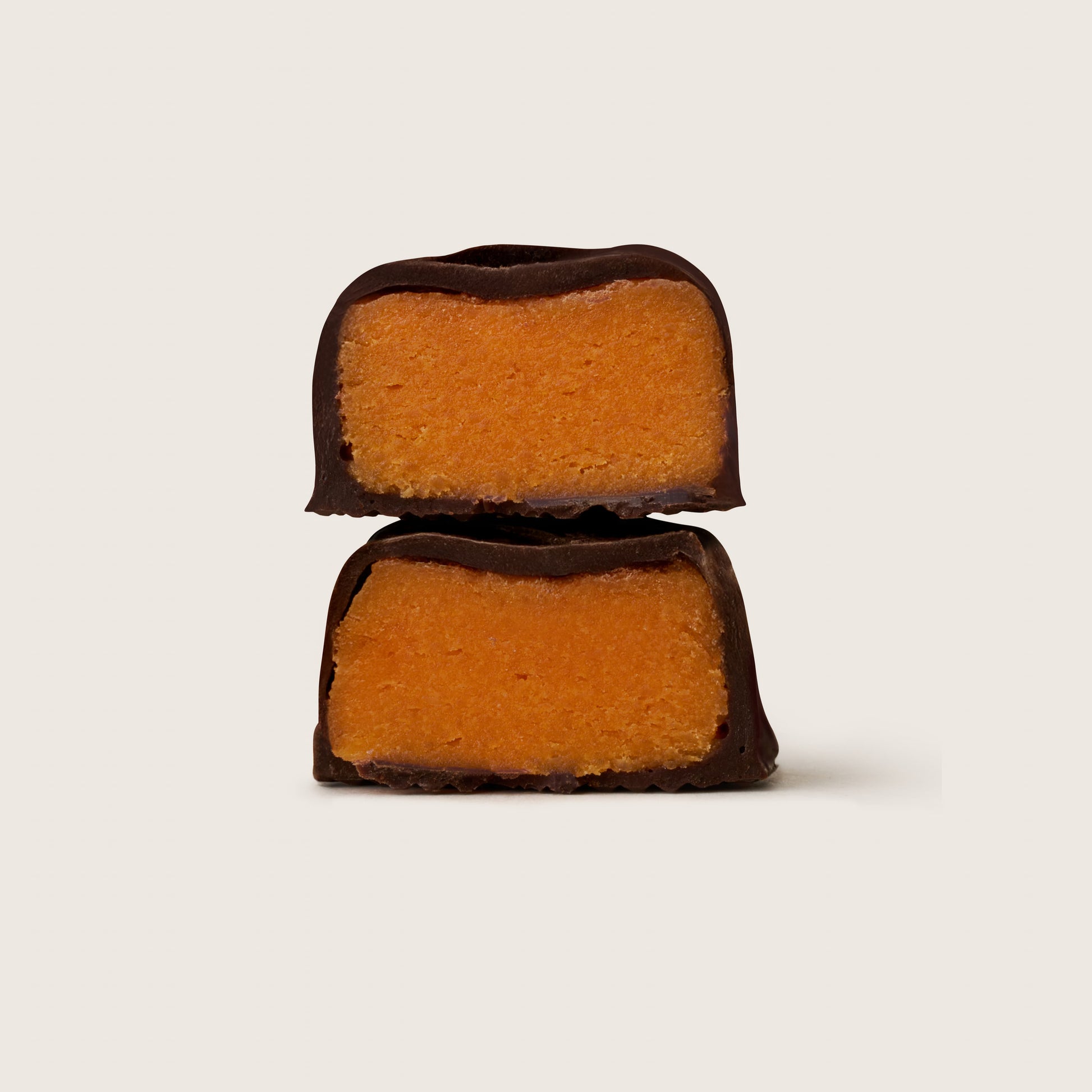Two chocolate-covered orange candies stacked on a light beige background