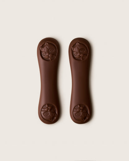 Two brown dog chew toys with cat face designs on a white background