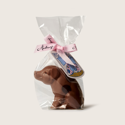 Chocolate pig figurine in clear packaging with a pink bow and tag on a light beige background