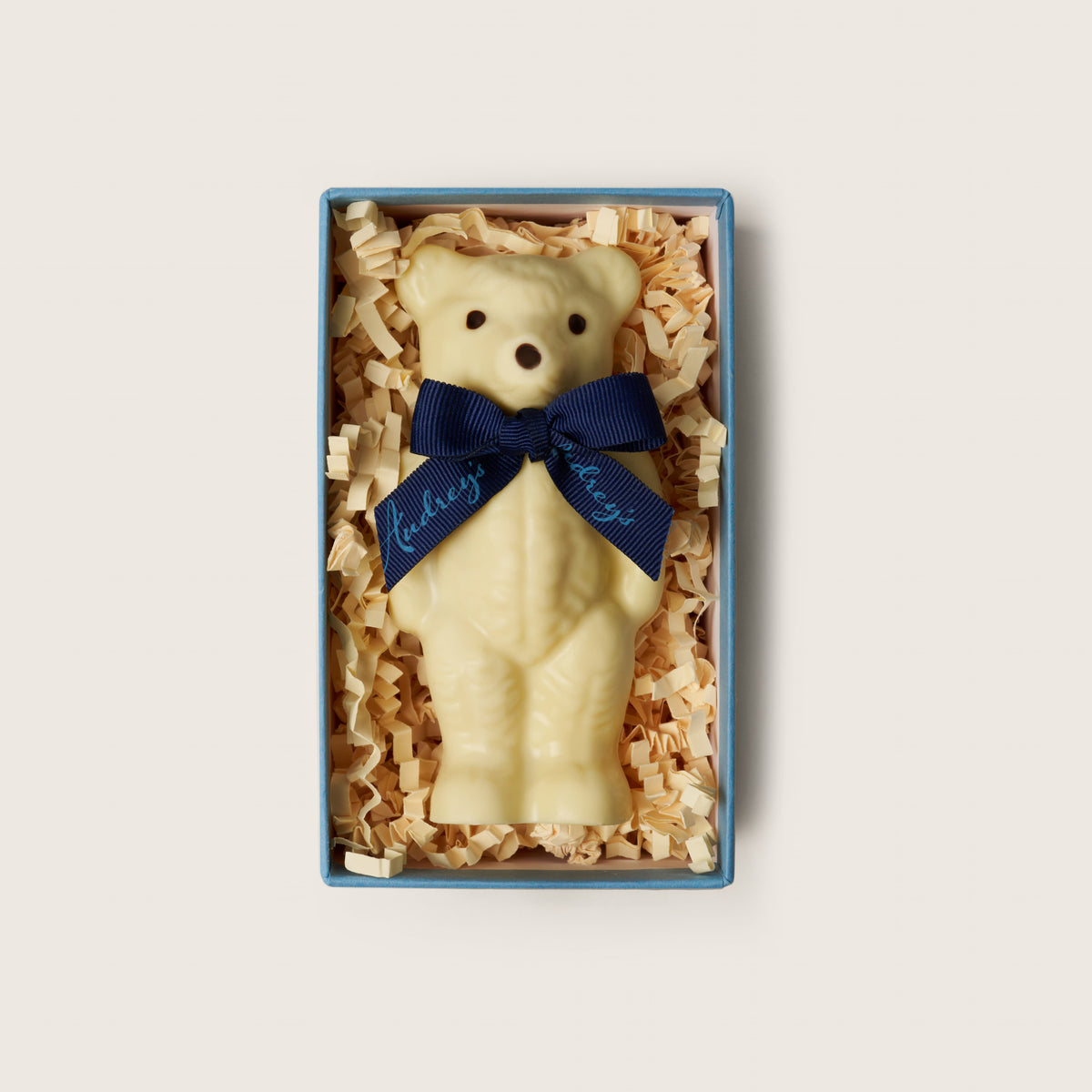 White bear-shape with a blue bow tie in a gift box on a light gray background