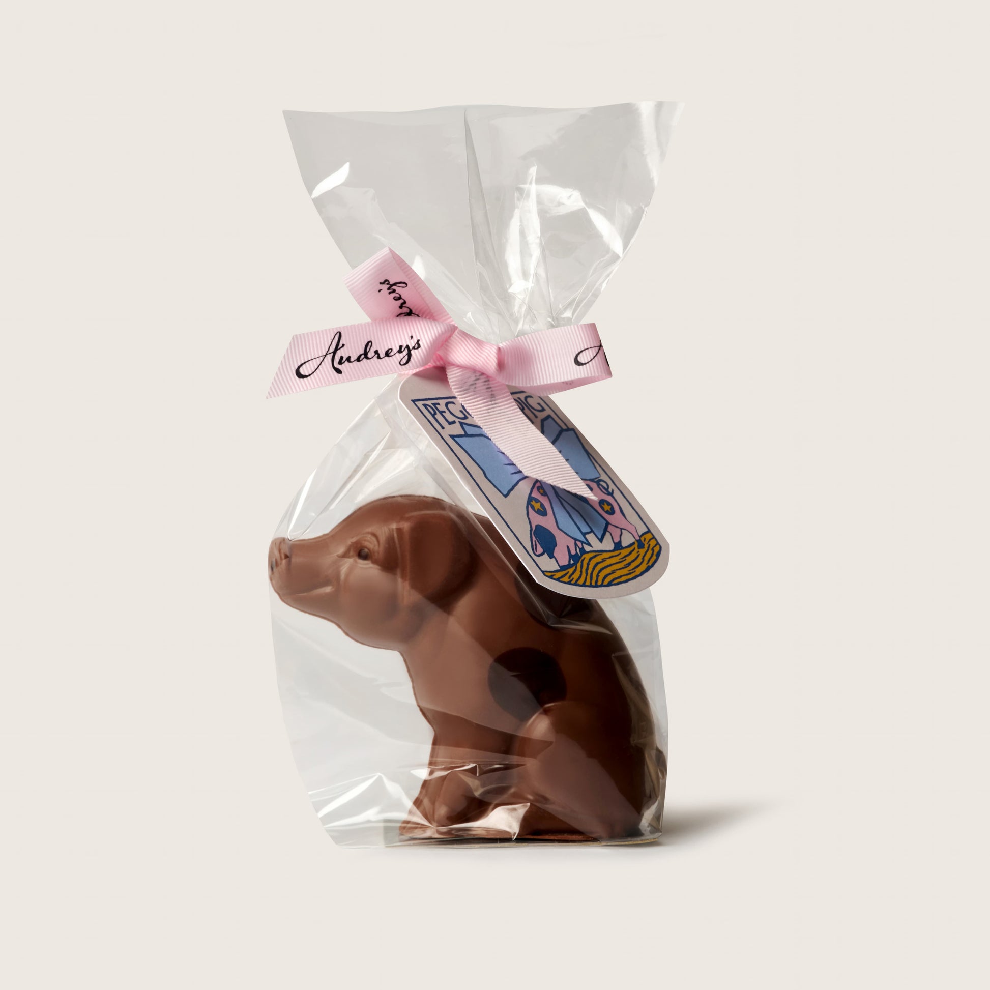 Chocolate dog figurine in clear packaging with a pink bow and label on a light gray background