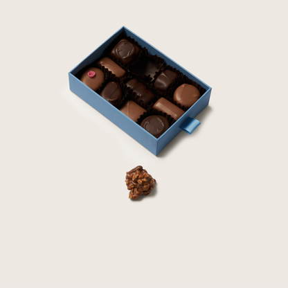 Open blue box of assorted chocolates with a single chocolate on a light gray background